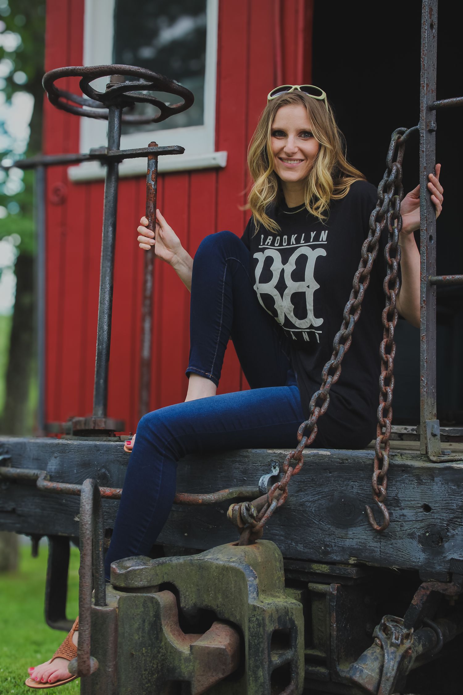 Woman in navy blue top sits casually on rustic playground equipment with metal chains in outdoor setting.