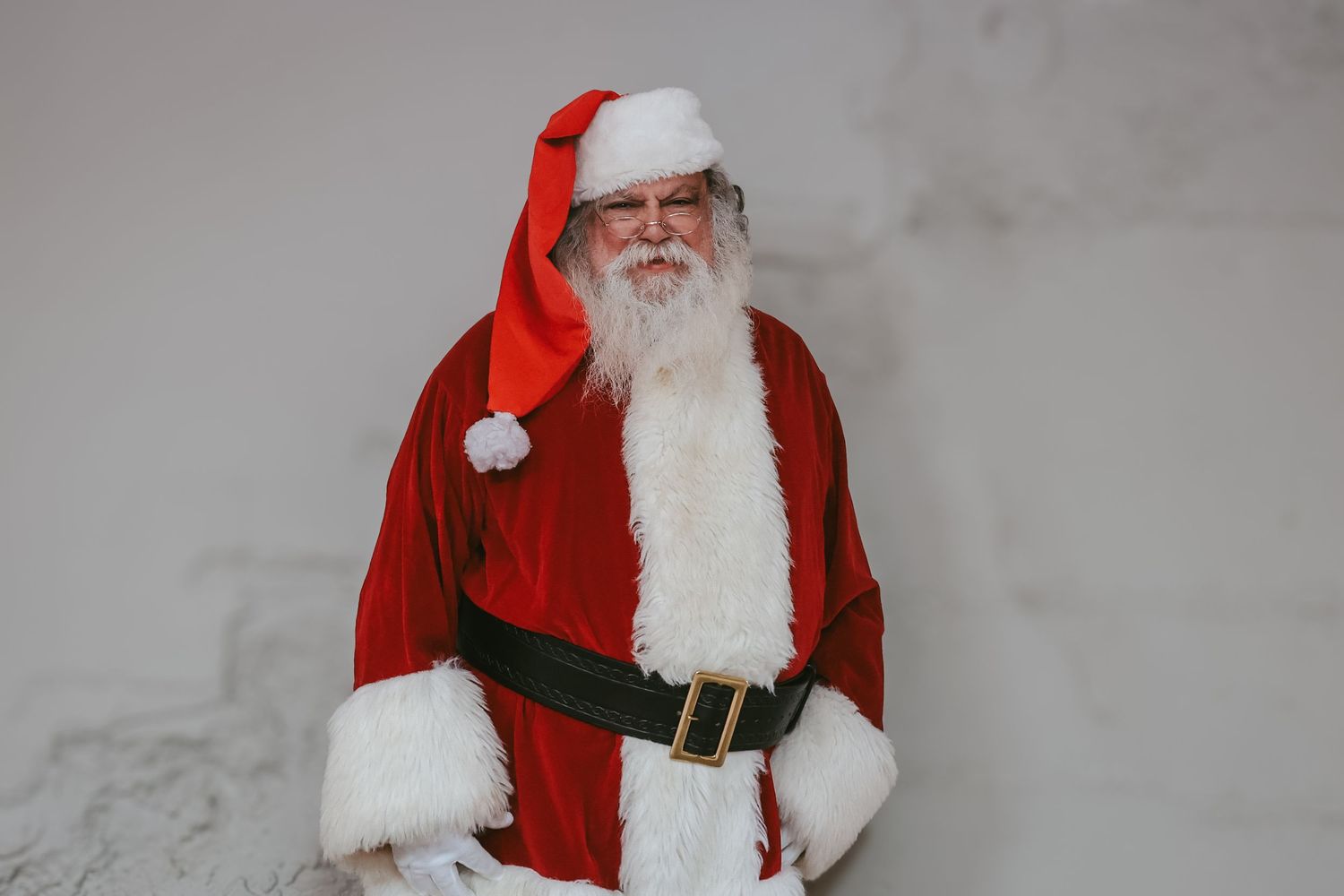 A person in a traditional red Santa Claus costume and white beard poses in multiple similar photos against a gray background.