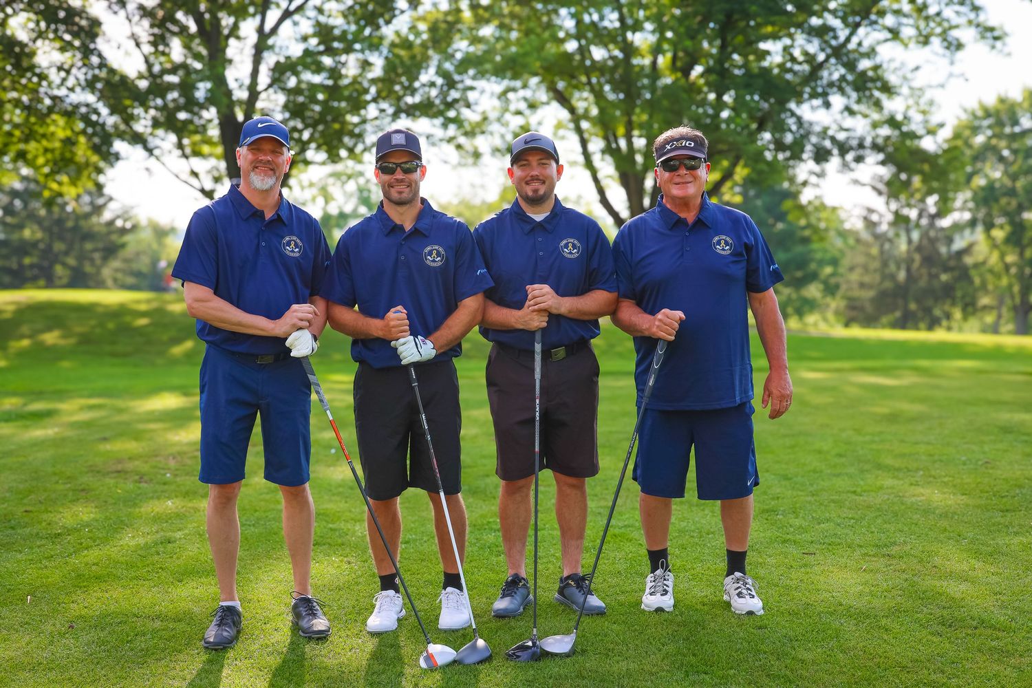 Group of golfers wearing blue shirts stand together on a lush green golf course during a tournament or event.