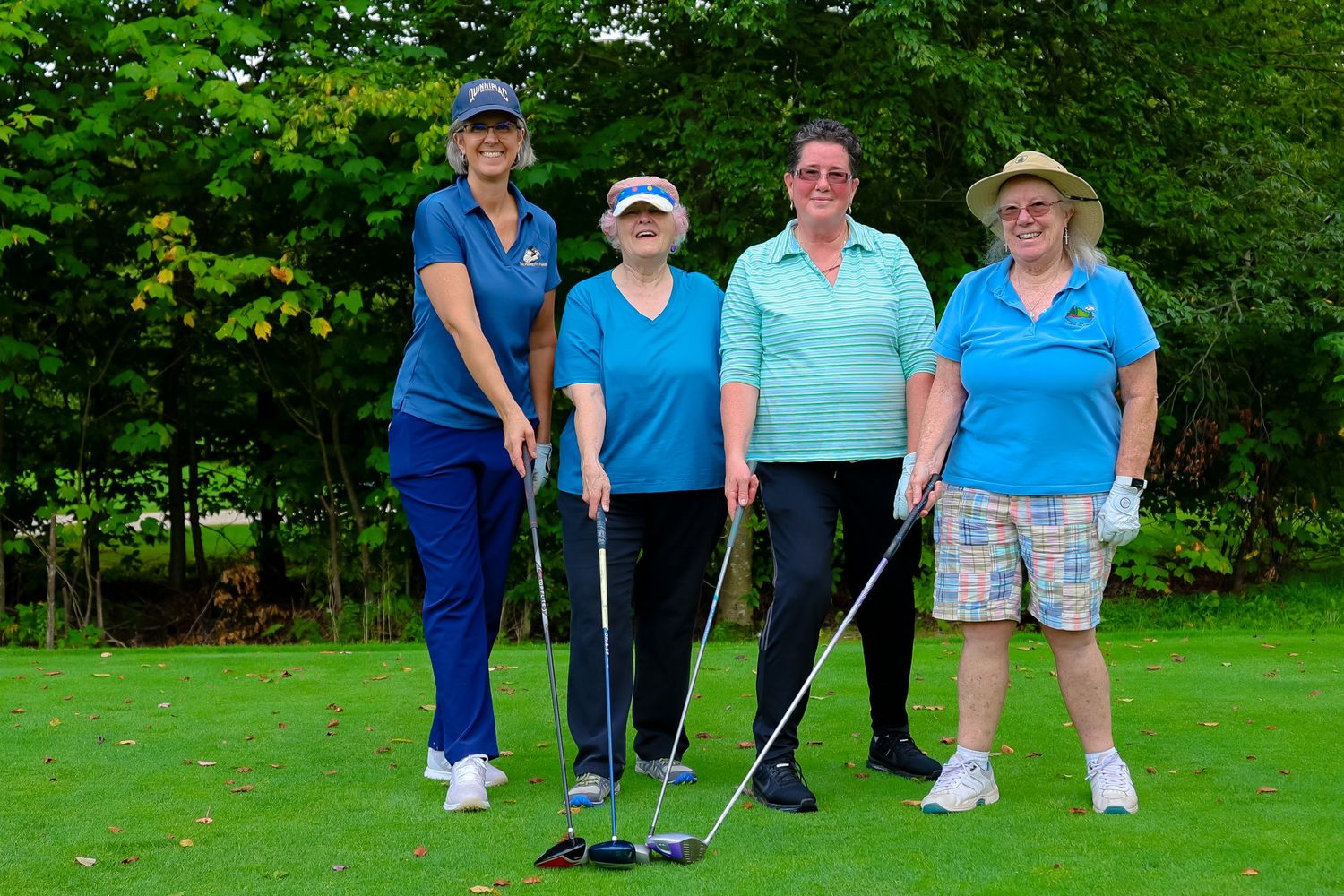 Four golfers in blue and white attire pose together with their clubs on a lush green golf course.