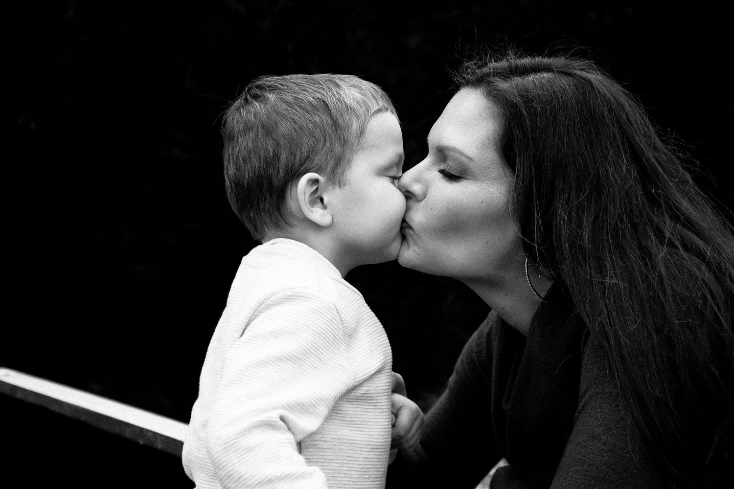 A black and white photo series shows tender moments between a parent and baby against a dark background.