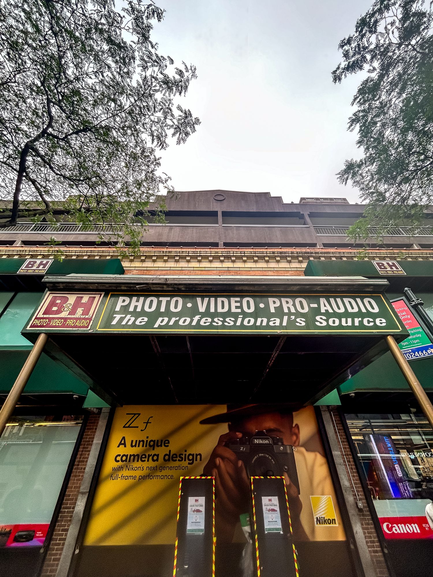 Storefront of B&H Photo Video Pro Audio store with green awning and yellow signage in an urban setting.
