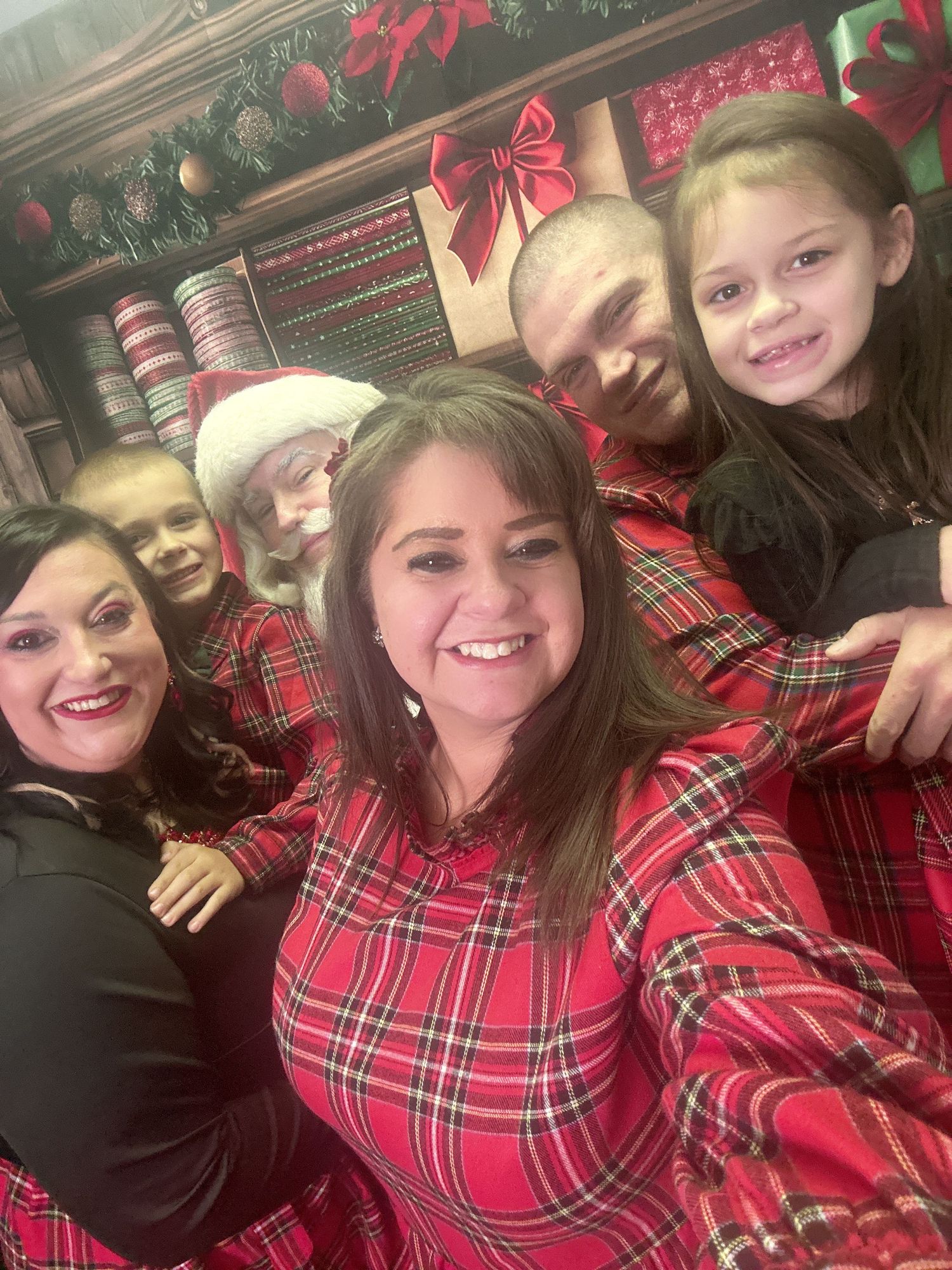 A group wearing matching red plaid holiday outfits poses together for a festive selfie with Christmas decorations in background.