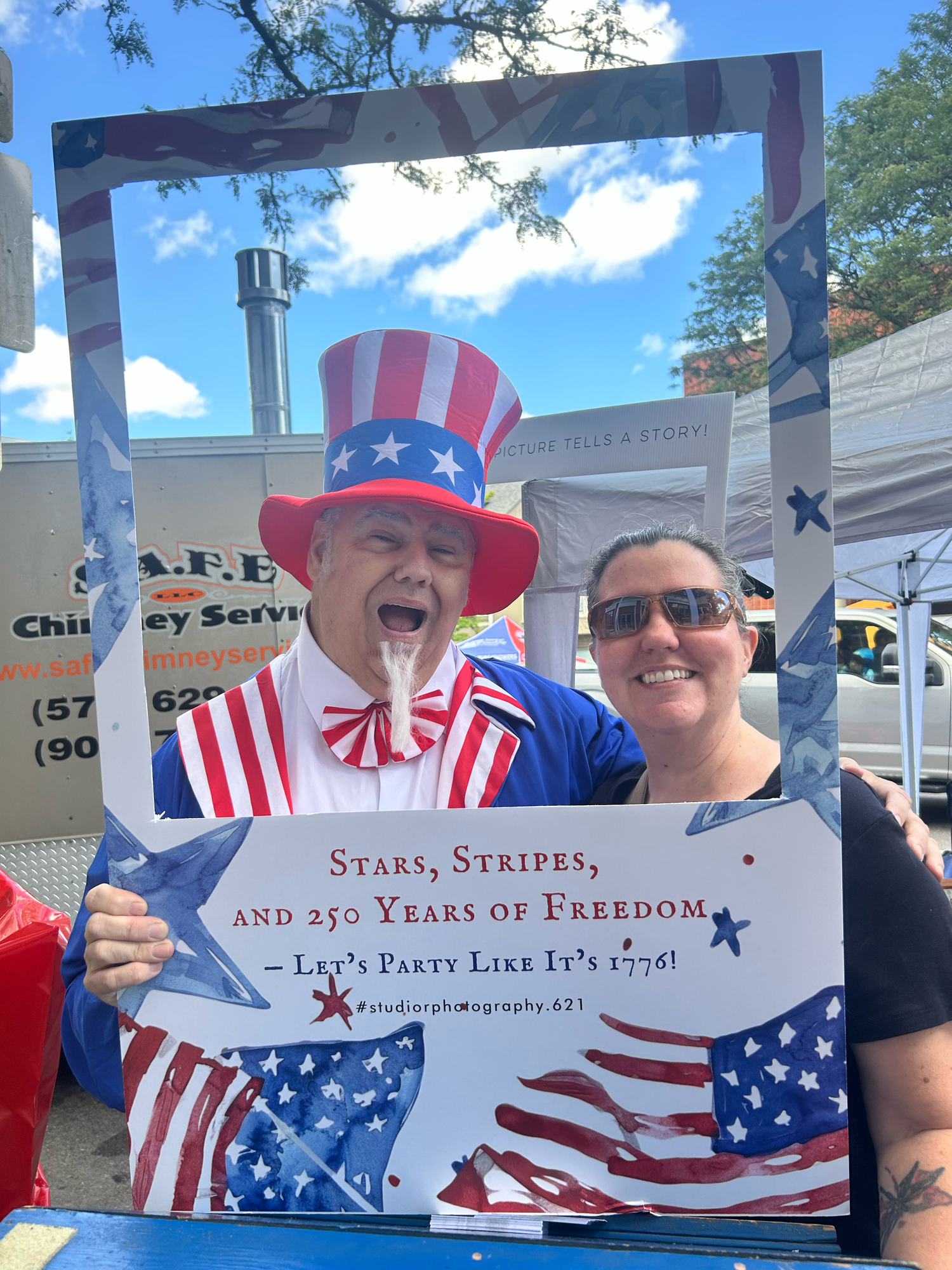 Patriotic crowd celebrates at outdoor event wearing American flag themed clothing and accessories under blue sky.