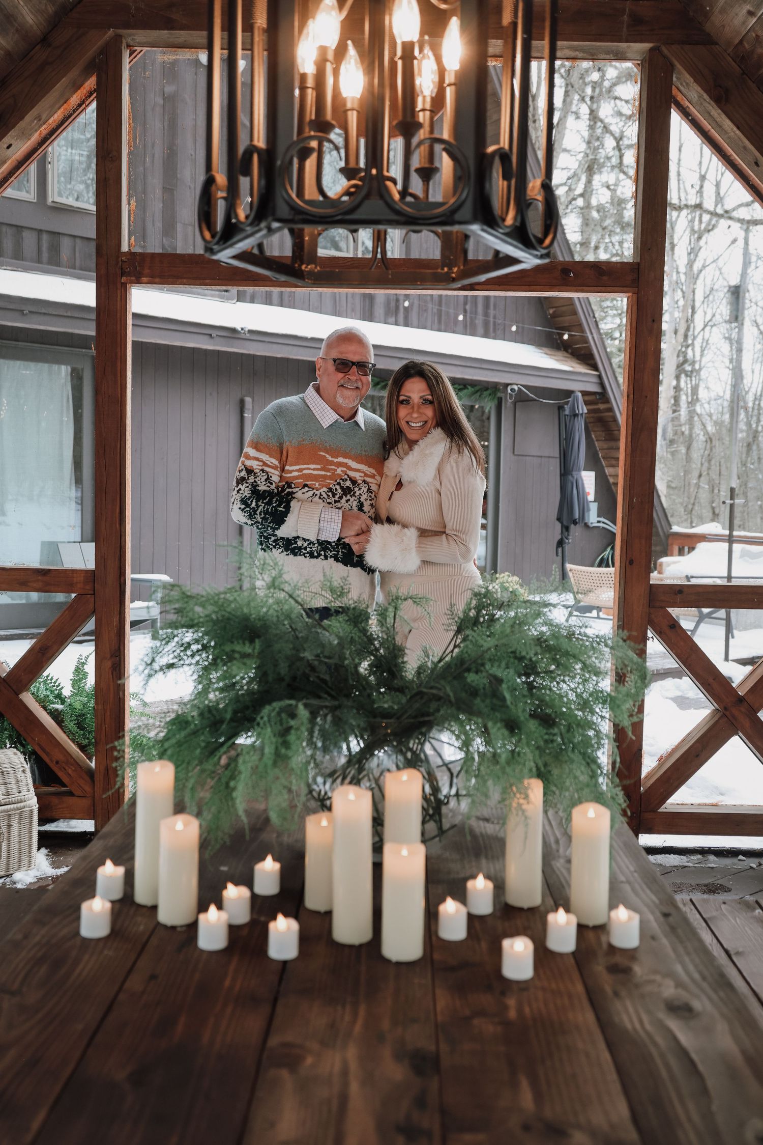 A rustic wooden table decorated with white candles and evergreen branches creates an elegant winter wedding atmosphere.