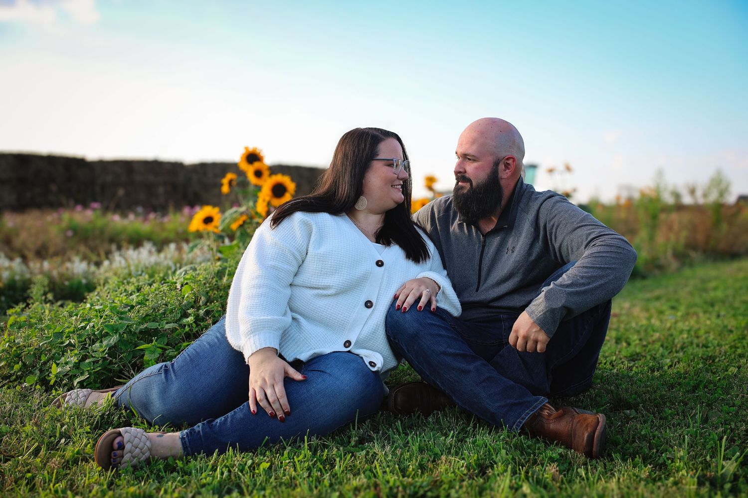 A couple relaxes together in a sunlit field with wildflowers during a romantic outdoor photo session.