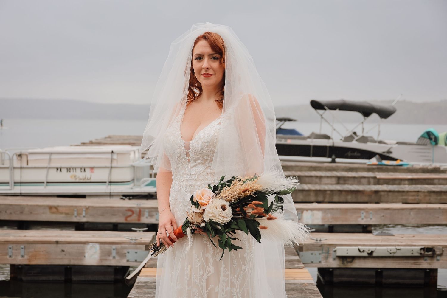 A bride in a white wedding dress holds a bouquet while walking along a beach at sunset.