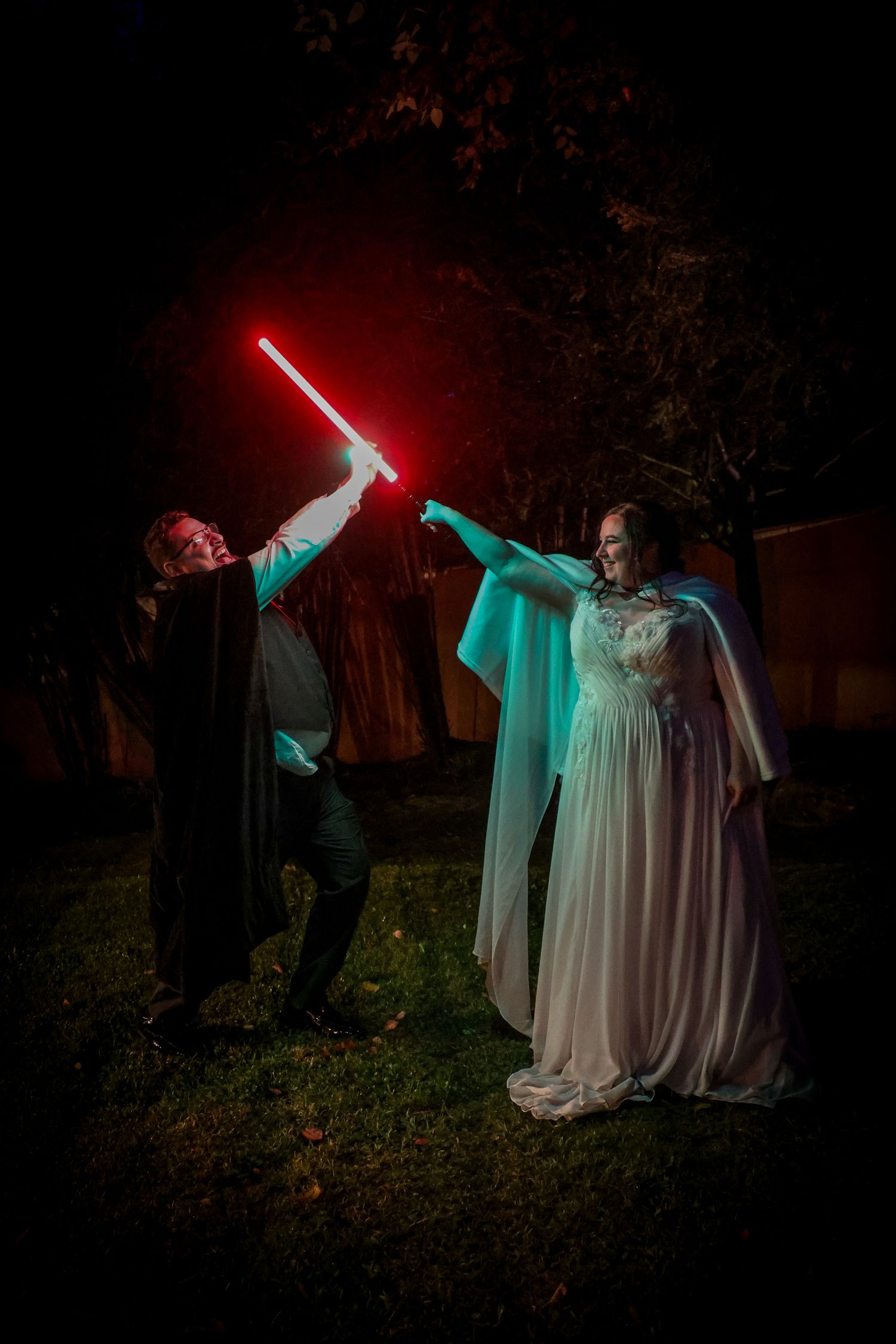 Two figures engage in a dramatic lightsaber duel in a dark outdoor setting with glowing red and green sabers.
