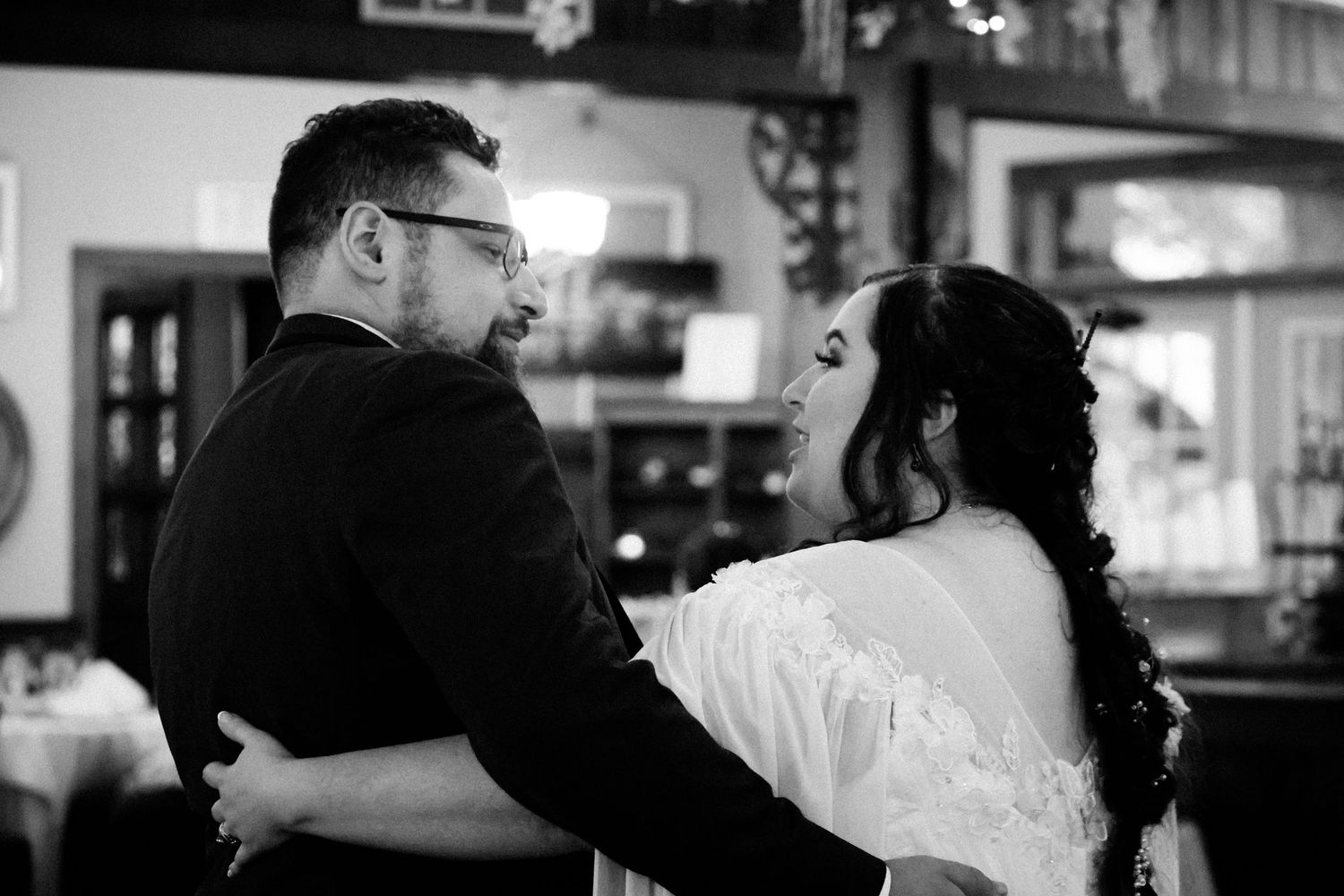 A black and white photo of a couple embracing and dancing together at what appears to be a wedding reception.