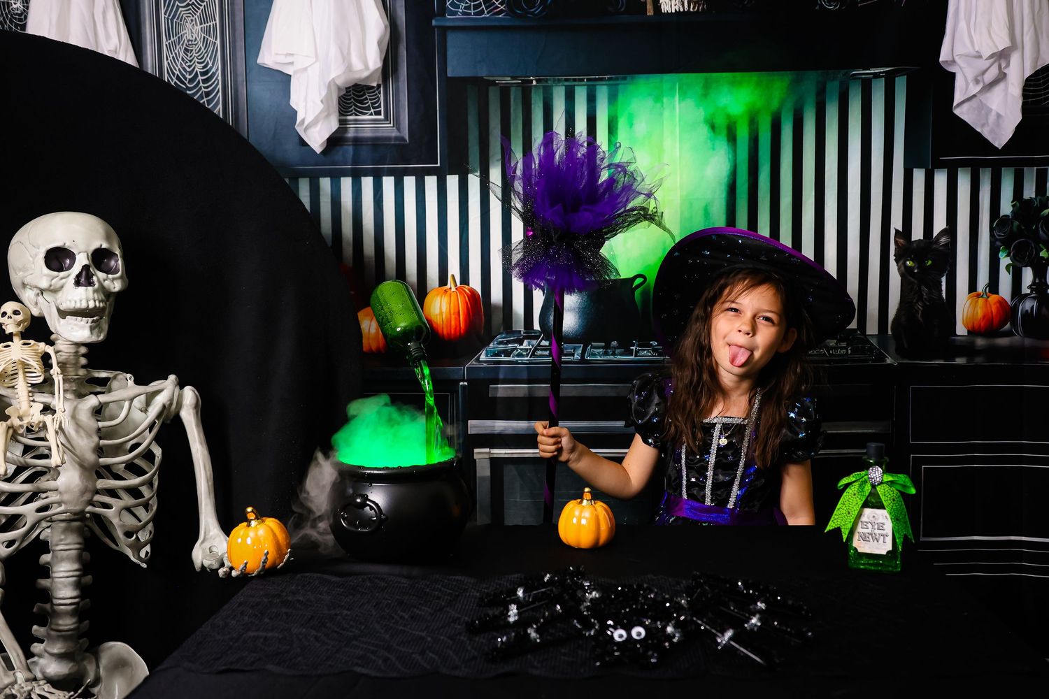 Halloween party scene with witch costume, skeleton decoration, pumpkins and spooky green lighting in a dark room.