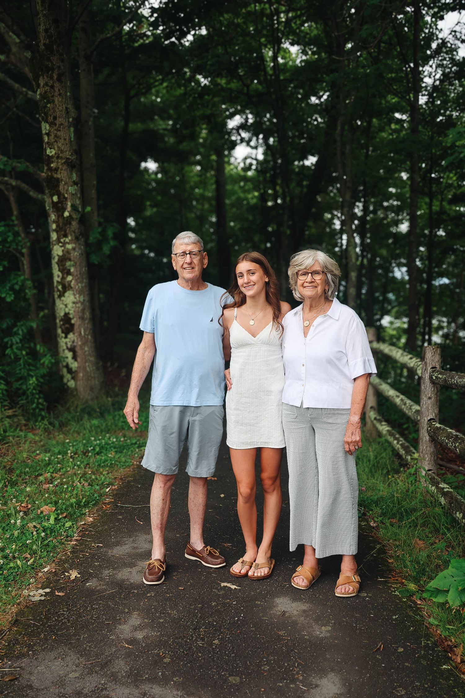 Elderly couple posing with young woman on wooded path in summer.
