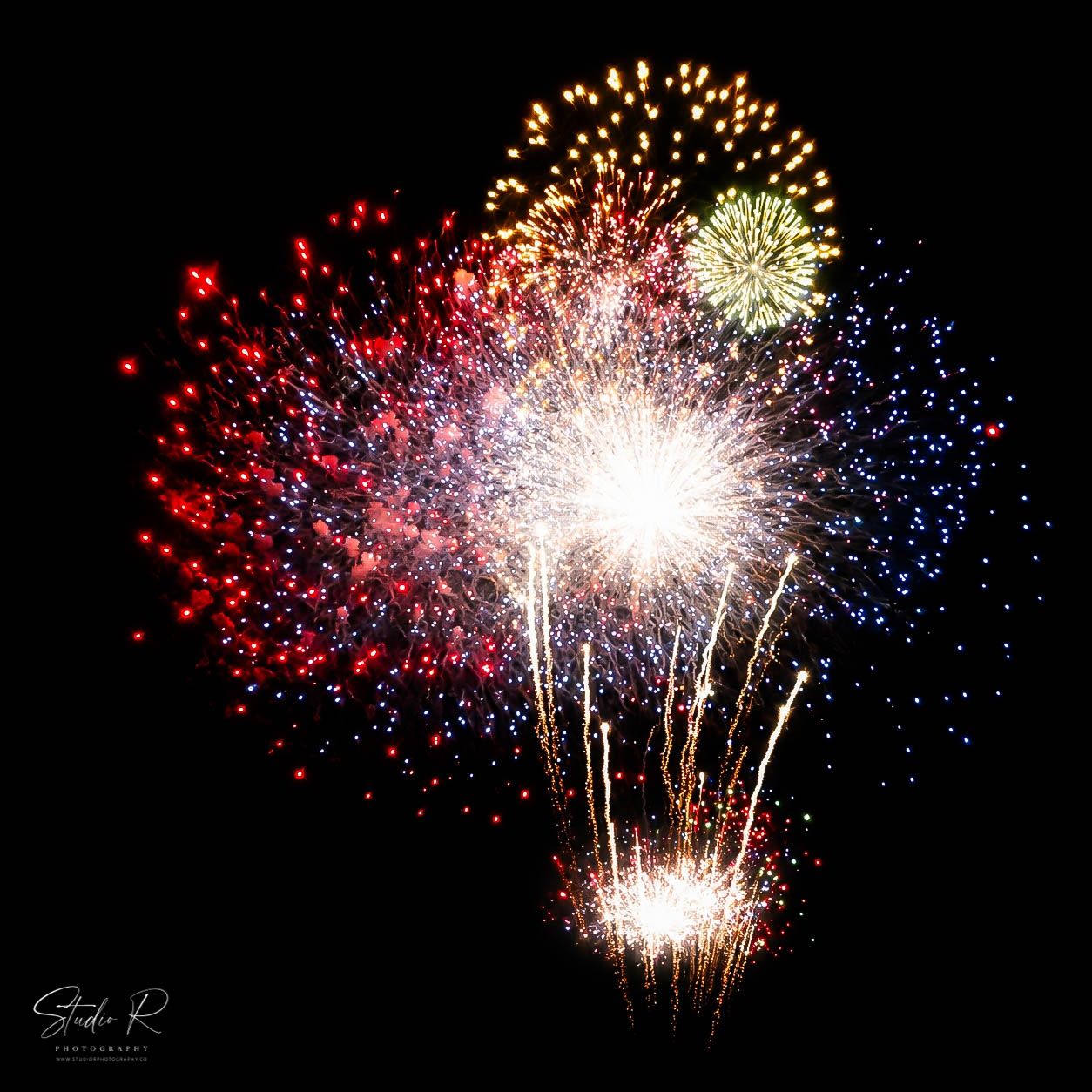 Colorful fireworks display with red, blue, and gold bursts against a dark night sky.