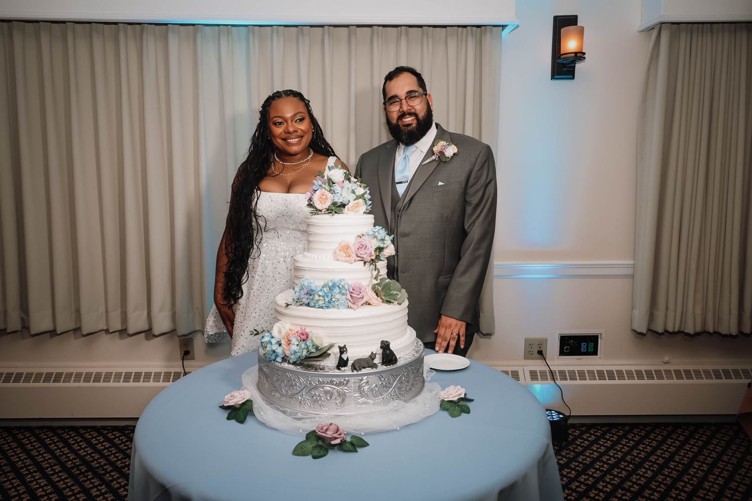 Newlywed couple cutting a elegant multi-tiered white wedding cake decorated with flowers at their reception.