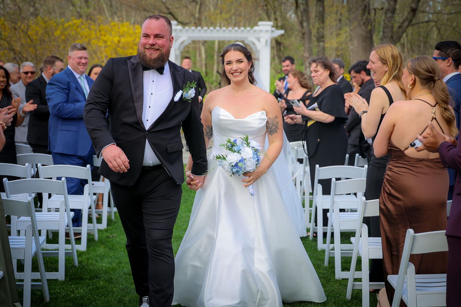 Bride and groom walk down the aisle hand in hand after outdoor wedding ceremony on lush green lawn.