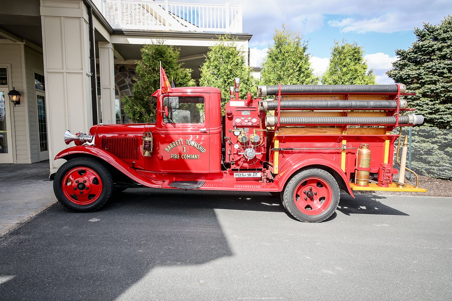 Vintage red antique fire truck parked in a lot, featuring classic design with wooden ladders and spoke wheels.