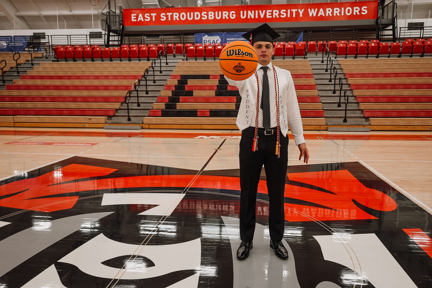 Student holding a basketball on the East Stroudsburg University Warriors court logo in the gymnasium.