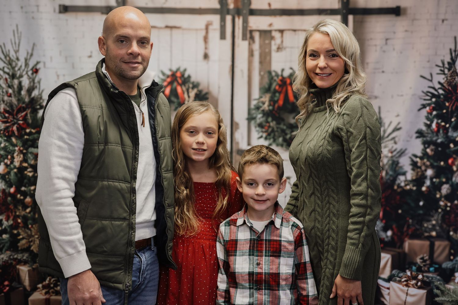 A family poses together in front of Christmas trees and decorations wearing festive winter attire.