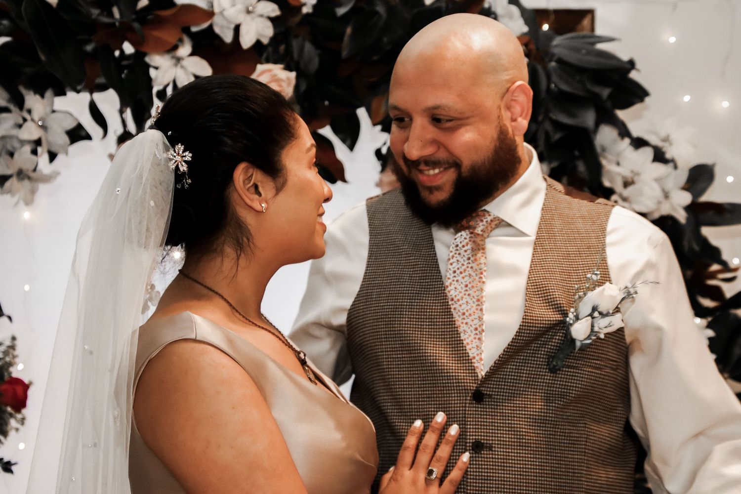 A happy couple embraces and laughs during their wedding celebration with decorative elements visible.