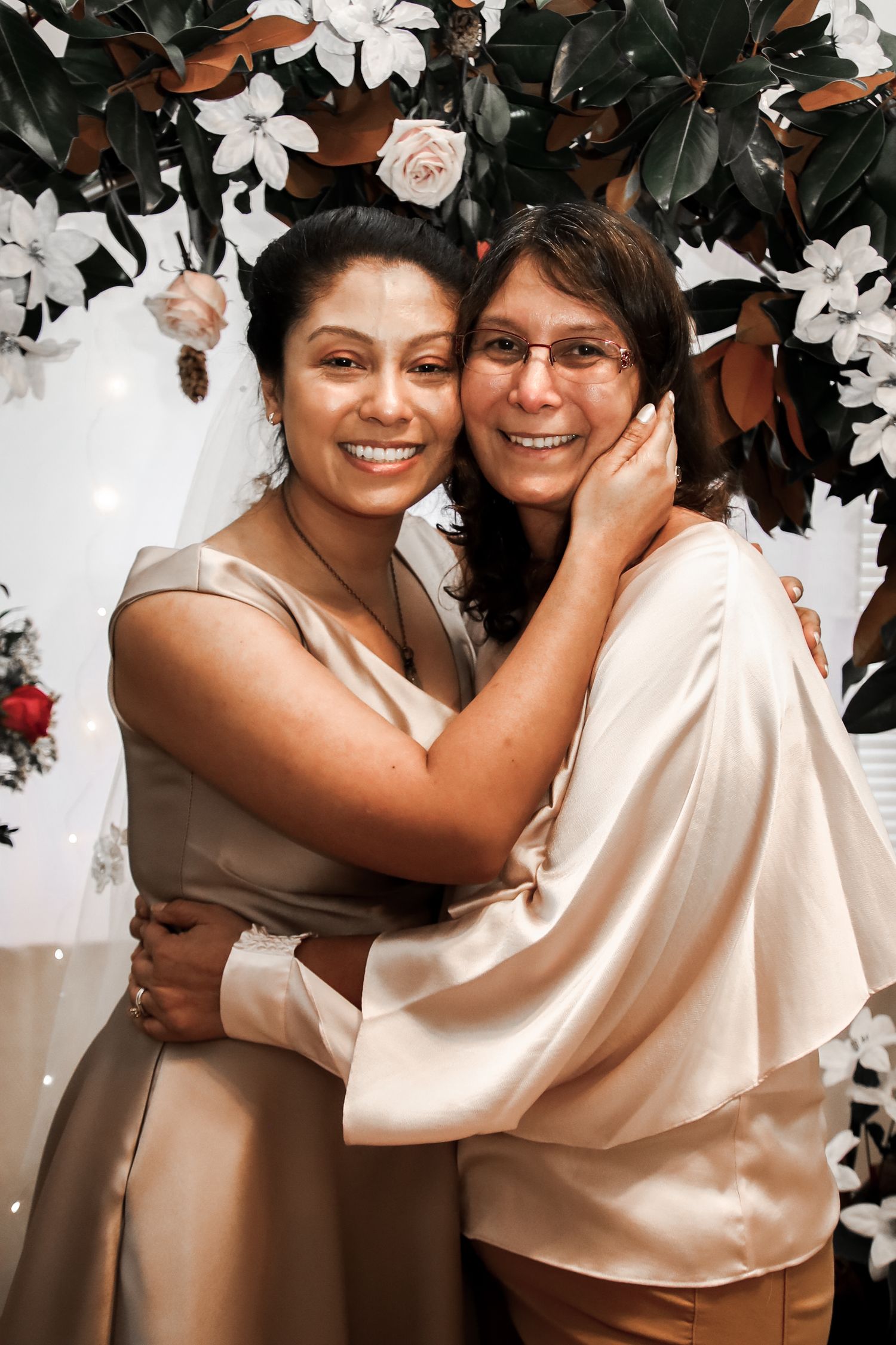 Four similar photos showing a warm embrace between two people in light-colored clothing against a floral background.