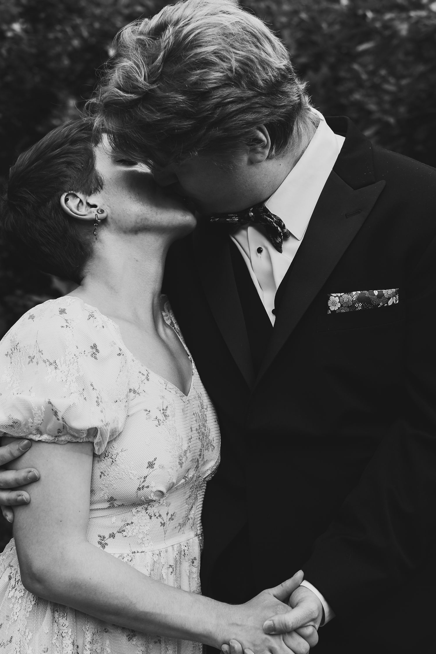 A romantic black and white photograph of a couple sharing an intimate kiss, with the bride in a lace dress and groom in a tuxedo.