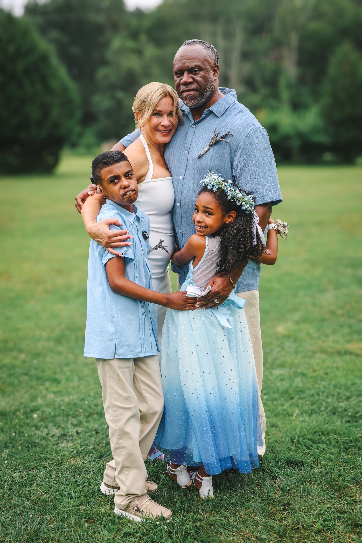 A family in coordinating blue and white outfits poses together on green grass during an outdoor photo session.
