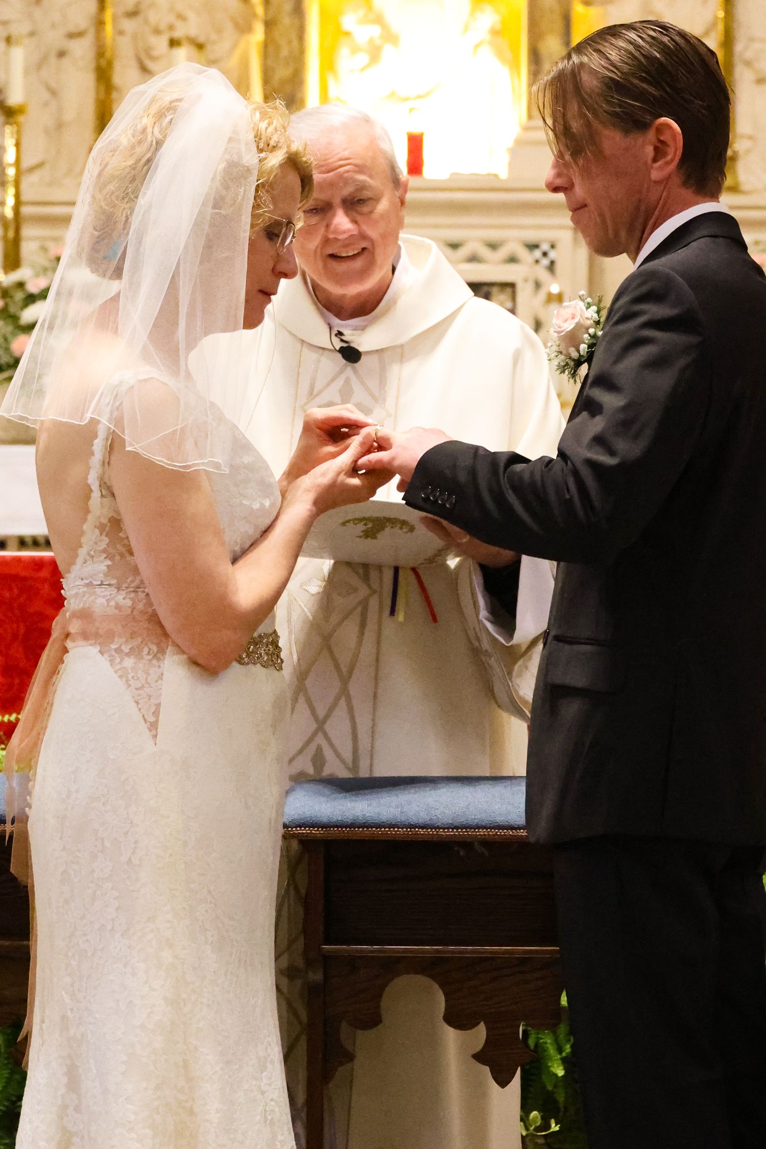 A traditional wedding ceremony takes place in an ornate church with a priest officiating the ring exchange.
