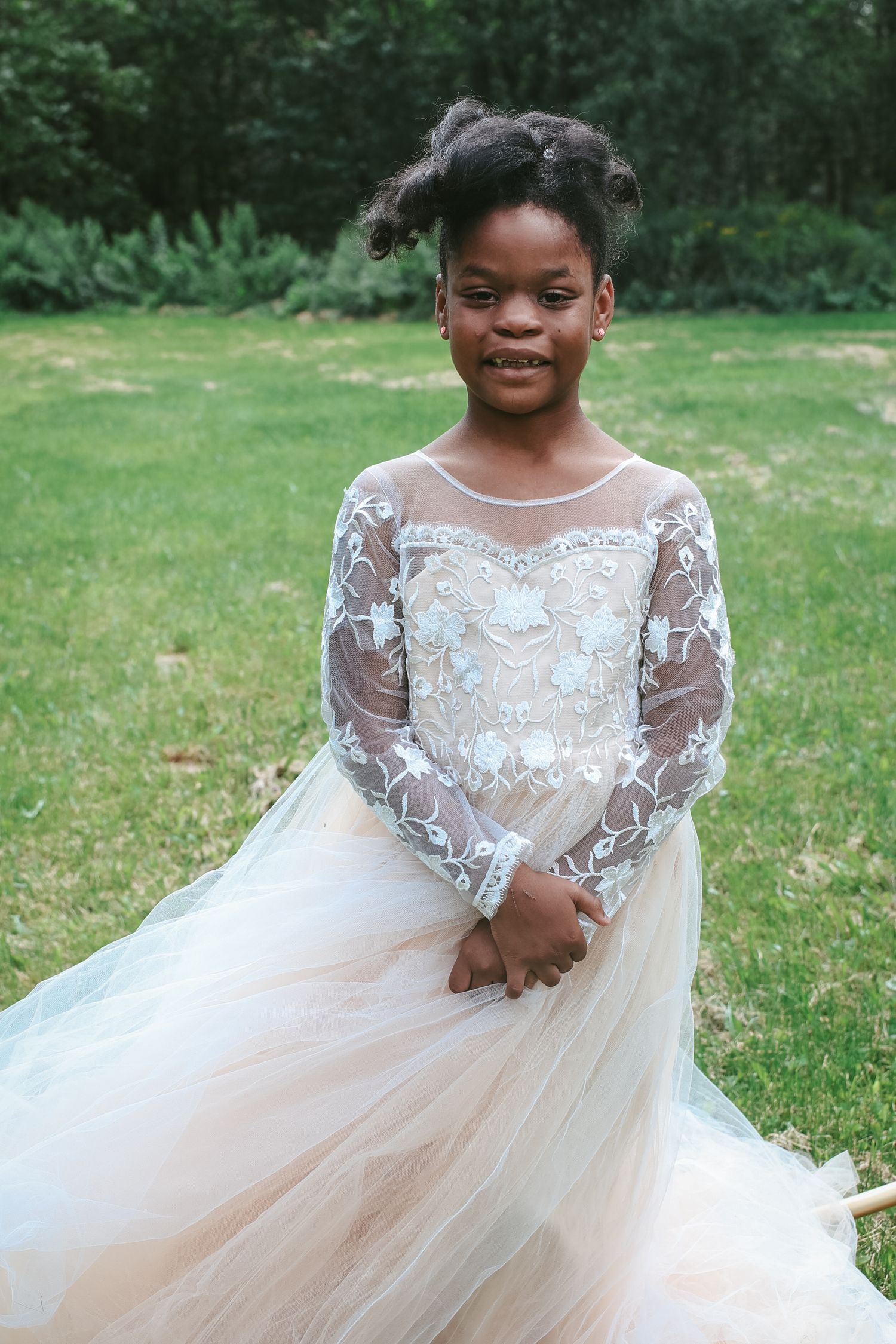 A beautiful formal gown in white with delicate lace sleeves and a flowing tulle skirt photographed outdoors.