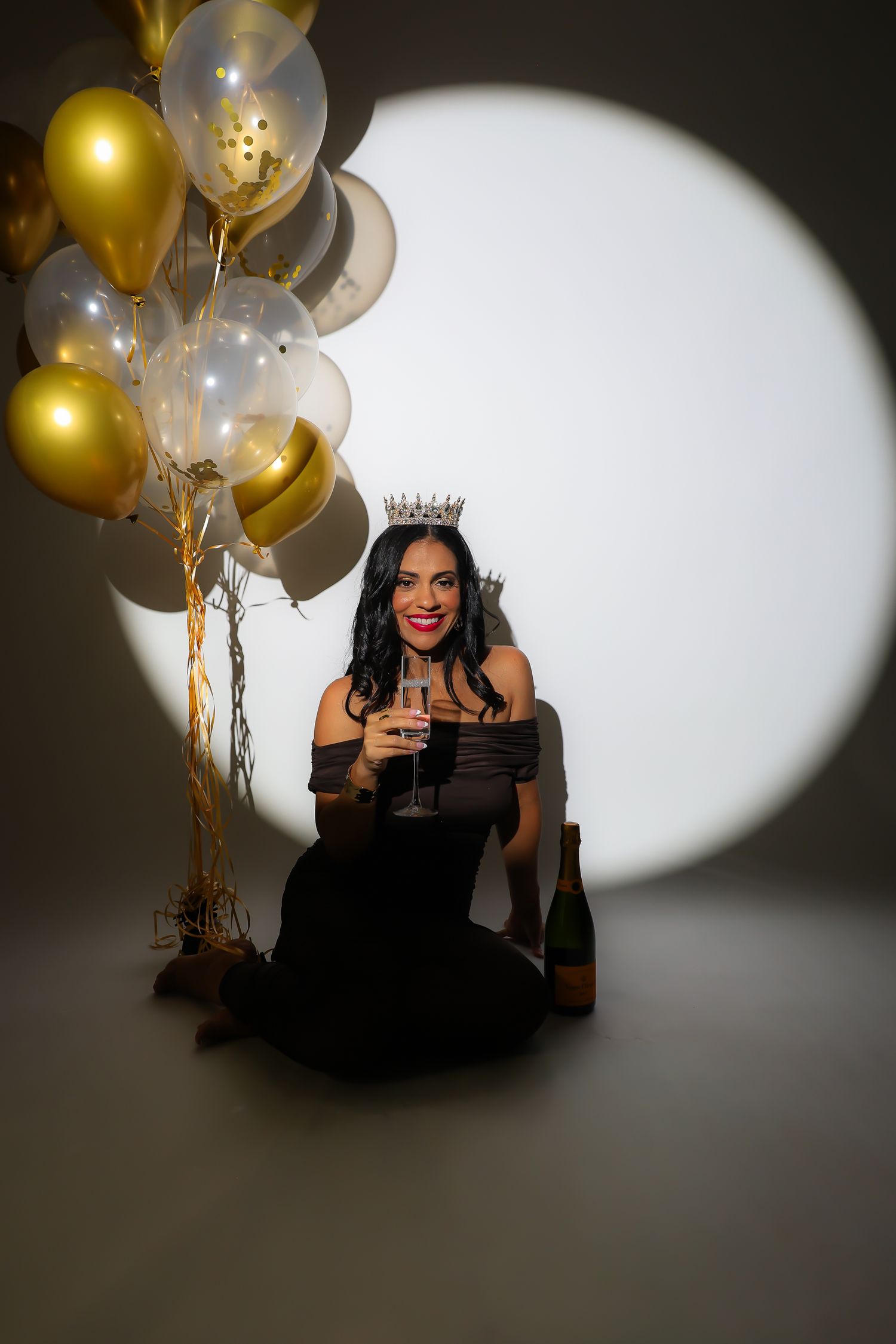 A celebratory photoshoot with gold balloons and dramatic lighting creates an elegant party atmosphere.