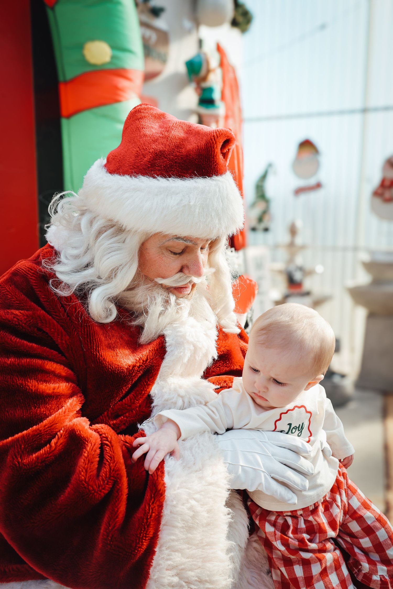 A heartwarming holiday scene shows Santa Claus interacting joyfully with a small baby in festive Christmas attire.