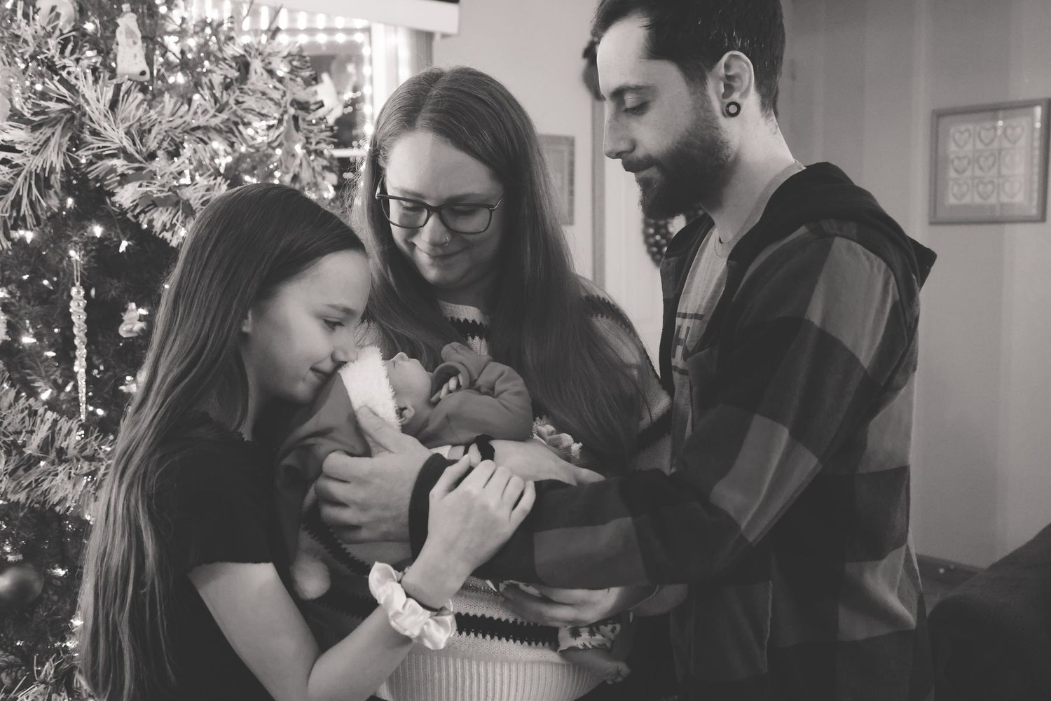 A group gathers around a newborn baby in a black and white photograph showing a tender family moment.