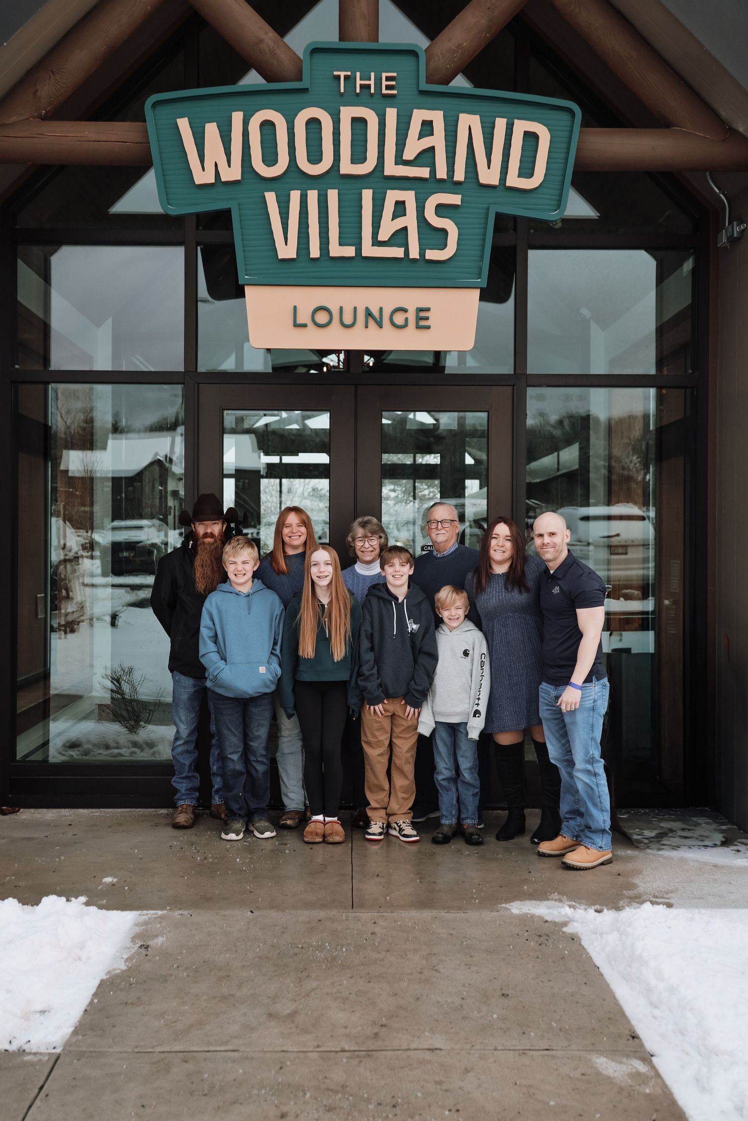 Group of people standing in front of a winter lodge entrance with snow on the ground and Woodland Villas signage visible.
