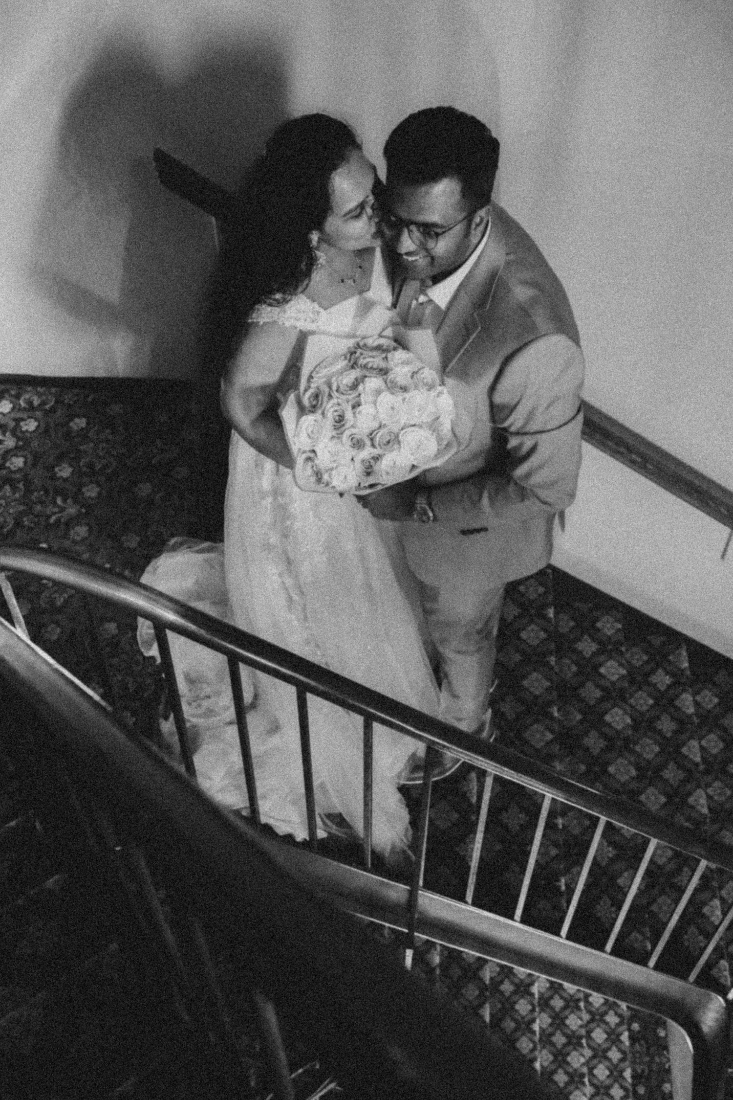 A sequence of black and white photos showing a couple descending a staircase with patterned carpet in a romantic embrace.