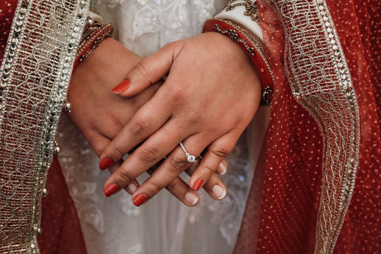 Close-up detail of hands with wedding rings against a sparkling red and silver sequined background.