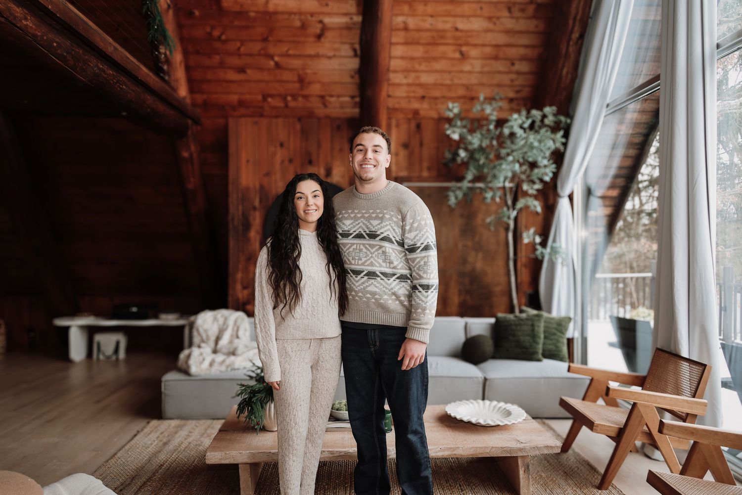 A couple stands together in a cozy cabin interior with wooden walls and modern furnishings.