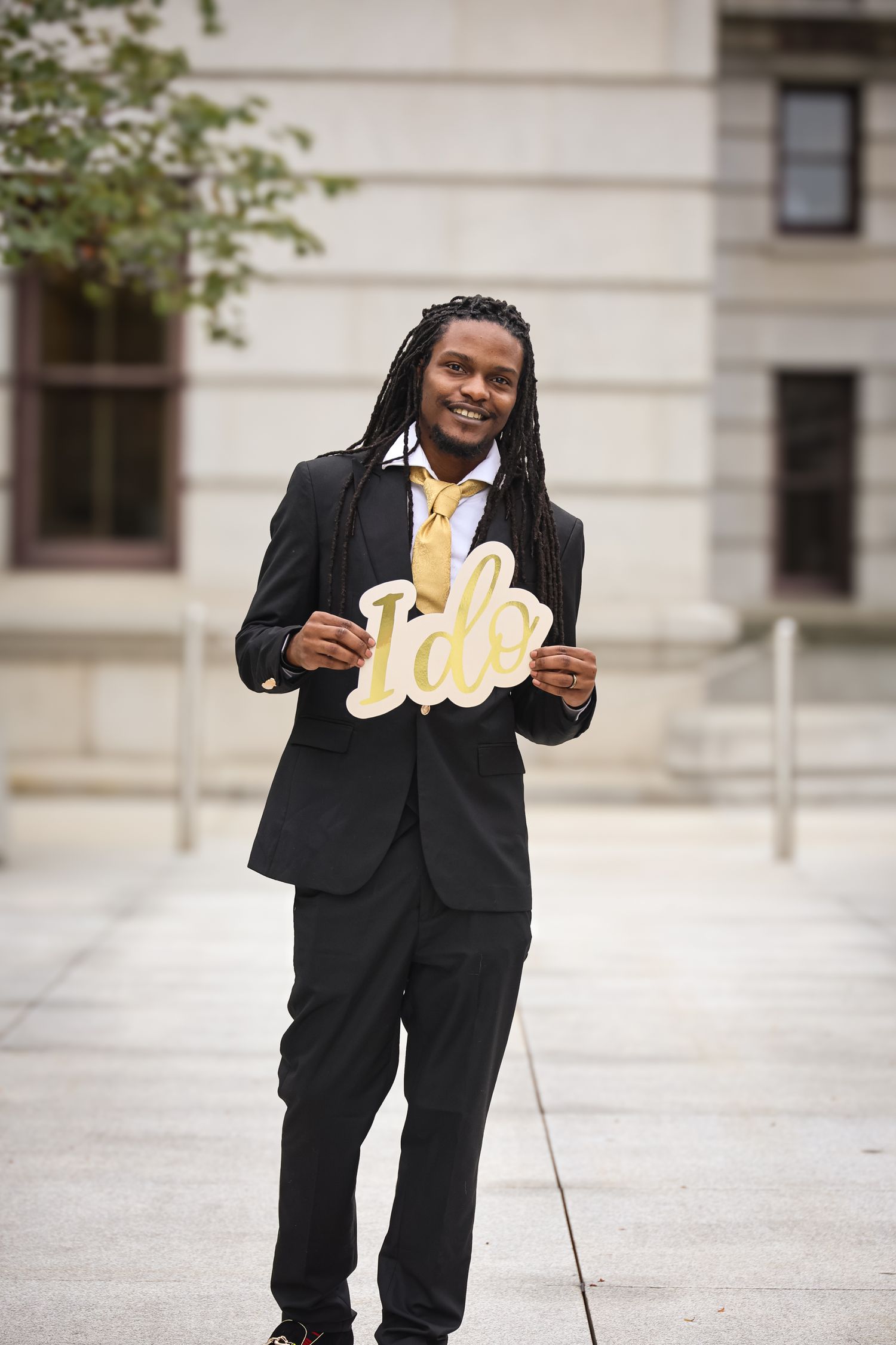 A person in a black suit and yellow tie smiles while holding a decorative gold 