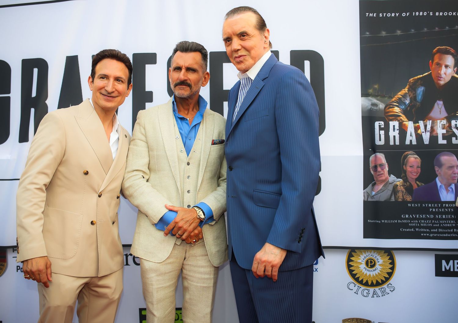 A group of men in tan and blue suits pose together at a movie premiere event.