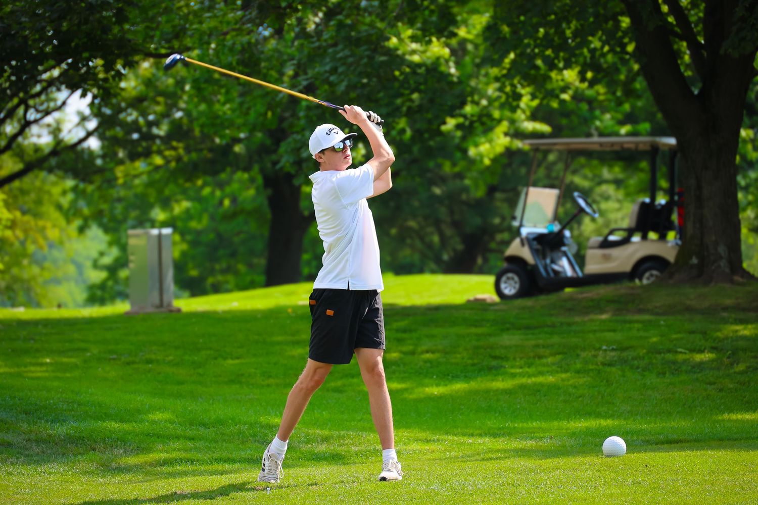 A golfer follows through on their swing with a club on a lush green golf course surrounded by trees.