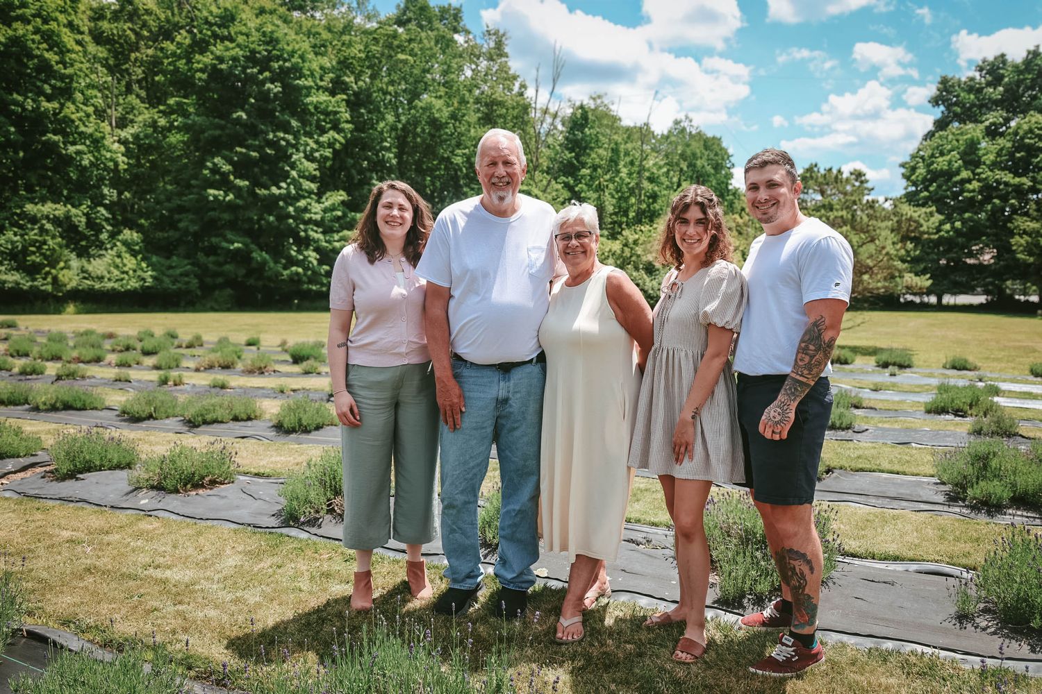 Family of five smiling together outdoors in a lavender field on a sunny summer day.