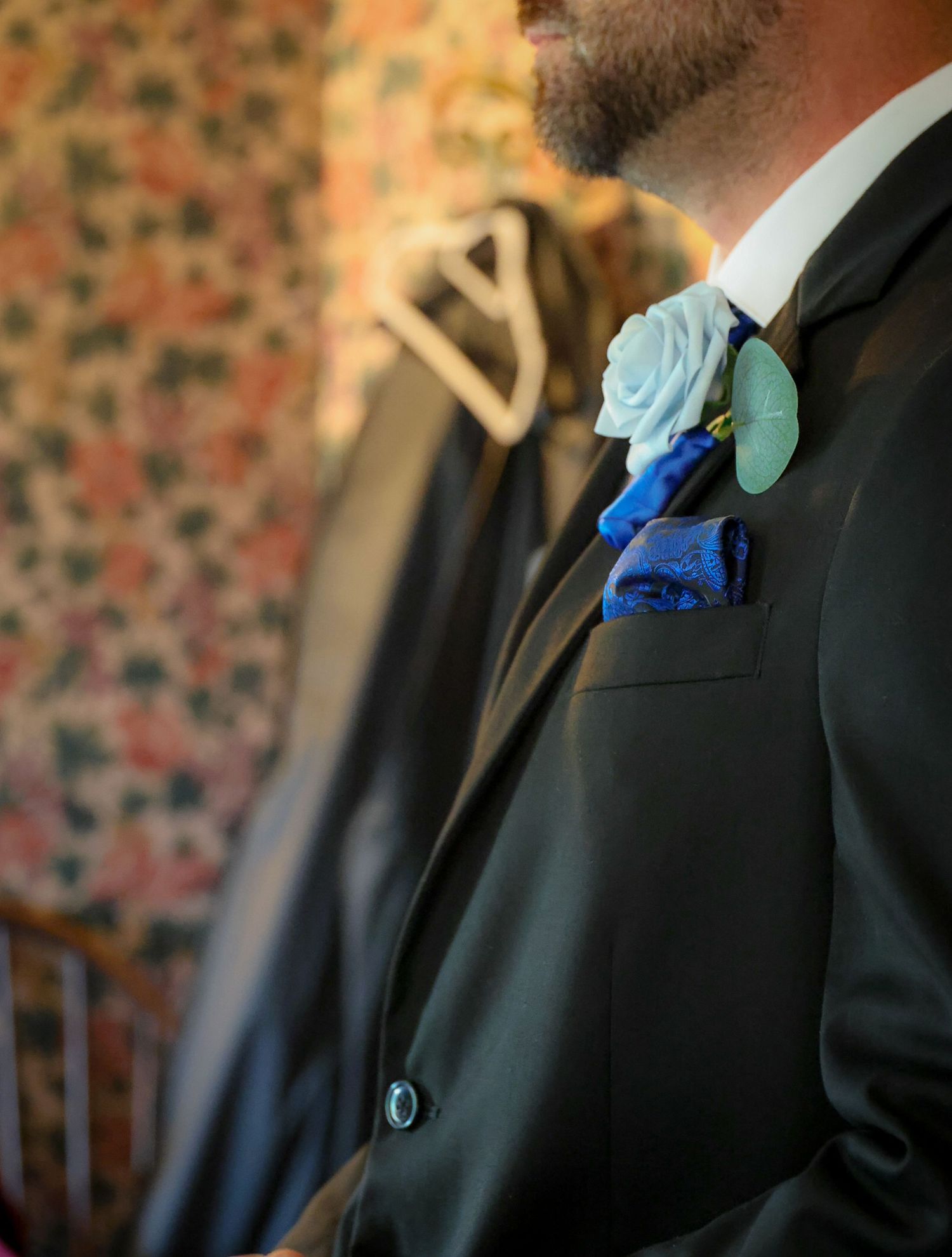 Groom in black tuxedo with light blue rose boutonniere and royal blue pocket square at wedding.