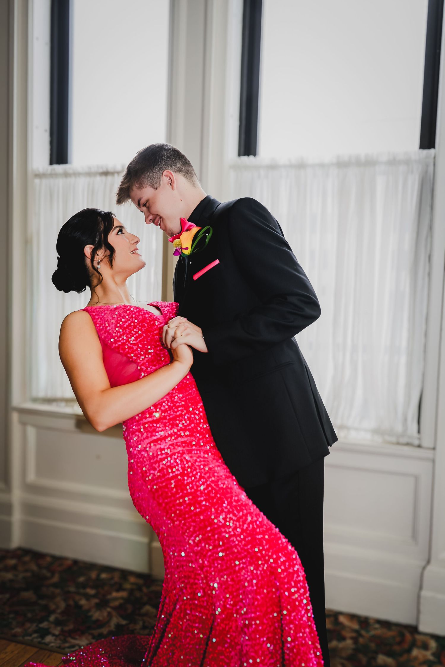 Couple in formal attire, woman in red sequin gown and man in black tuxedo, sharing a romantic dance pose.