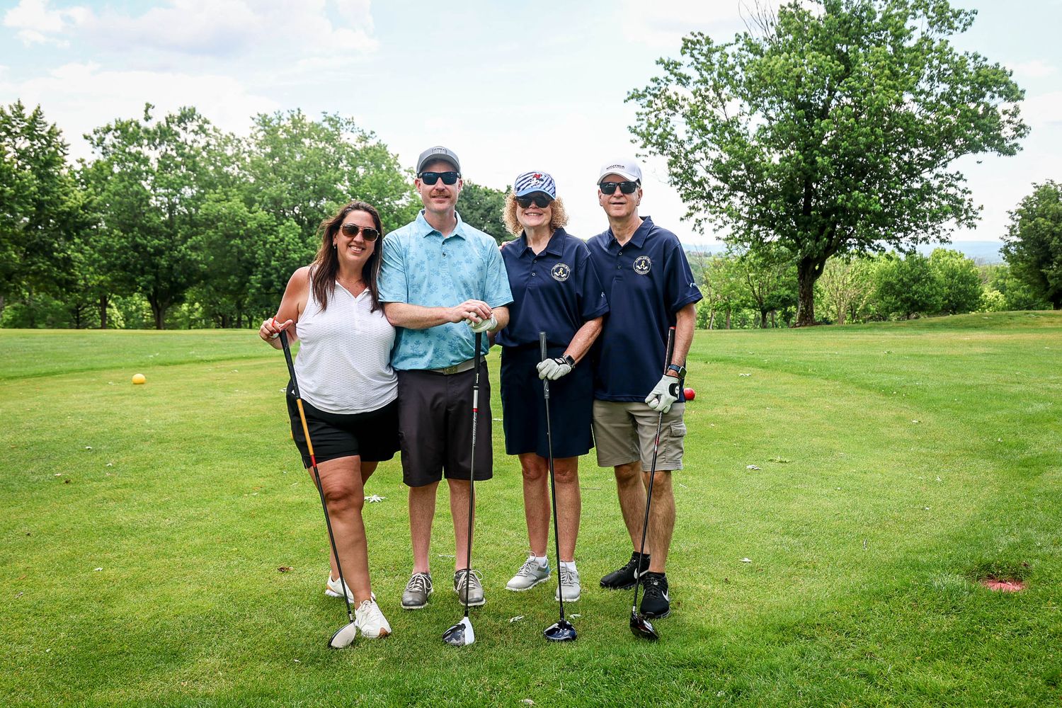Four golfers posing together on a lush green golf course on a cloudy day.