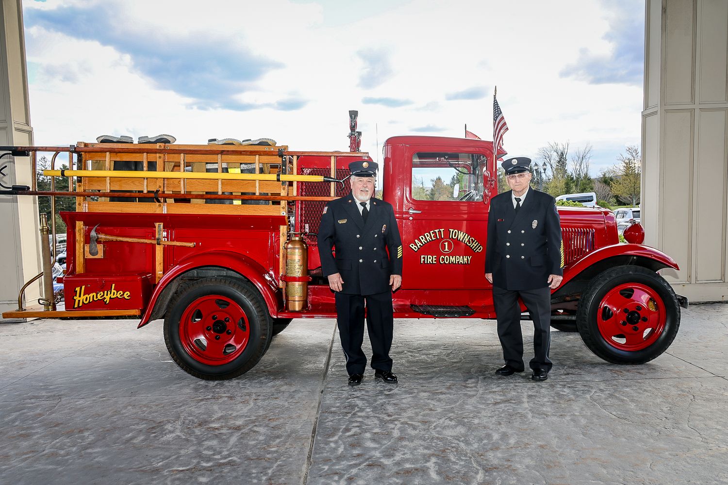 Two firefighters in uniform stand proudly before a vintage red Harriett Township Fire Company truck outside a station.