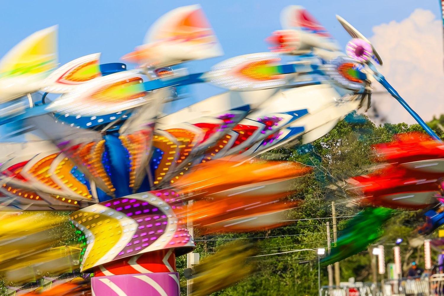 Colorful carnival ride spinning with motion blur, showcasing vibrant rainbow-colored decorations against a blue sky.