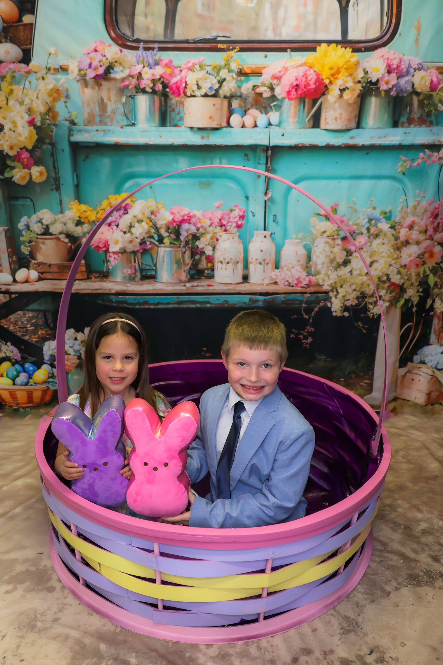 Children pose in a colorful Easter photo setup with vintage turquoise truck, pink basket and spring flowers.