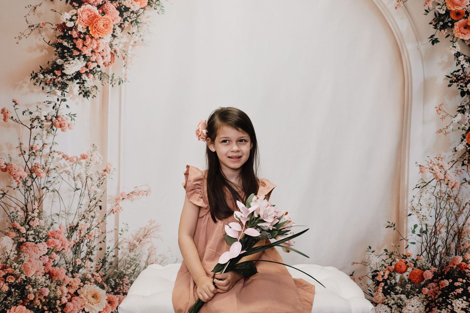 A floral photo session setup with peach and coral flowers against a light beige wall creates a romantic spring atmosphere.