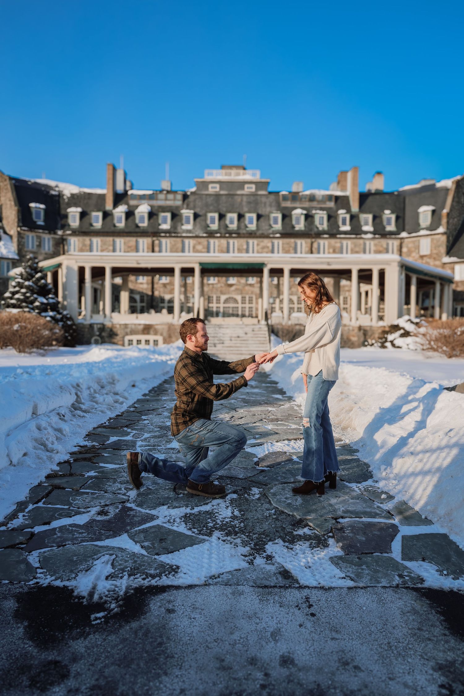 Two people playfully throw snowballs at each other in front of a grand historic mansion on a winter day.