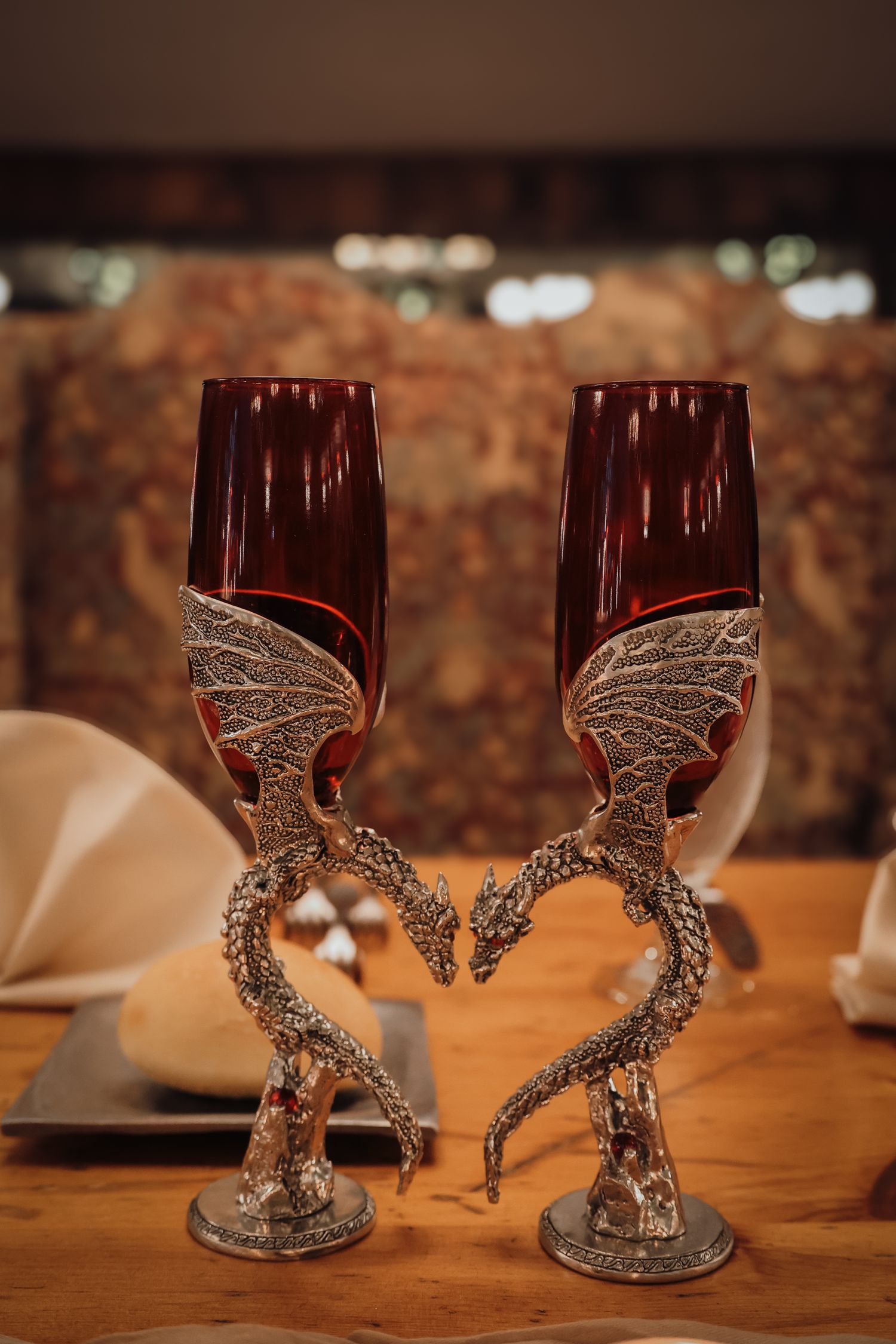 Decorative wine glasses with intricate dragon-shaped pewter stems displayed on a wooden table in warm lighting.