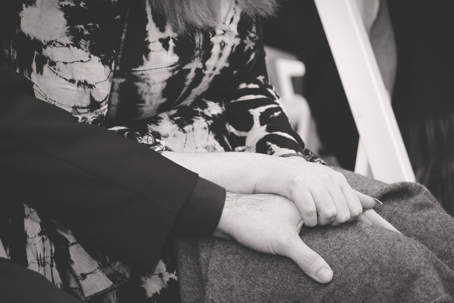 A close-up black and white photograph shows a hand resting gently on a textured fabric surface.