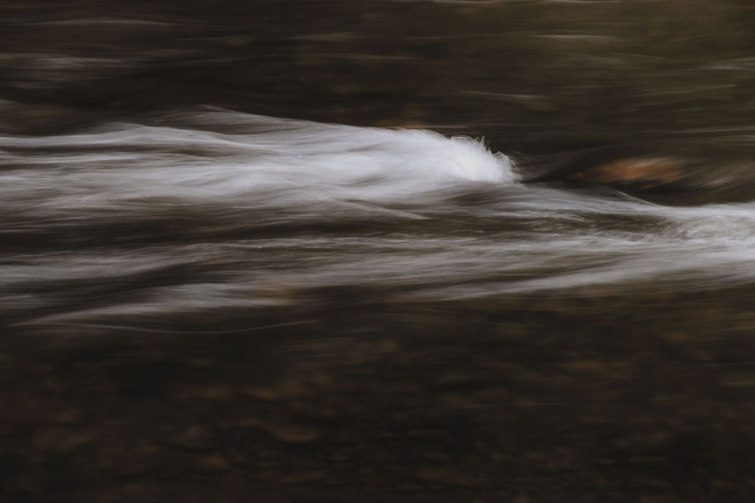 Long exposure photograph of flowing water creating smooth white streaks against a dark background.