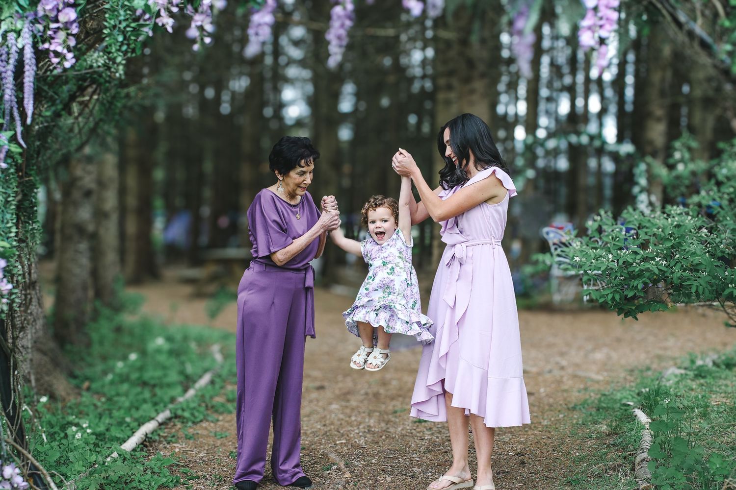 Three people in coordinating purple and pink outfits enjoy quality time together on a forest path.